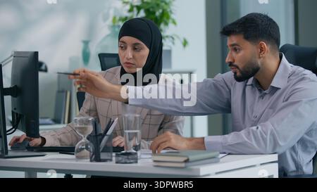 Two business colleagues in office talking with computer working. Arabian businessman leader boss consulting helping to Islamic Muslim woman Stock Photo