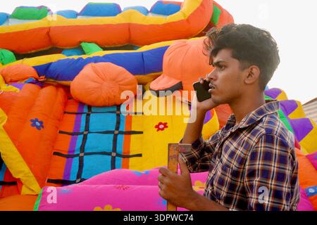 Young Indian man talking on mobile phone beside colorful inflatable bounce house in Alappuzha, Kerala, India Stock Photo