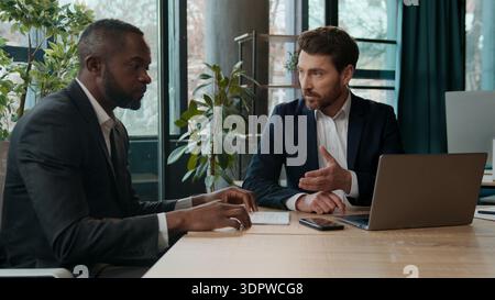Diverse business team two businessmen Caucasian African American men with laptop documents review in office working colleagues discuss data analyzing Stock Photo