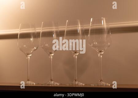 Row of empty wine glasses placed on a wooden shelf in a restaurant or bar interior under warm soft lighting. Clean transparent glassware creates an el Stock Photo