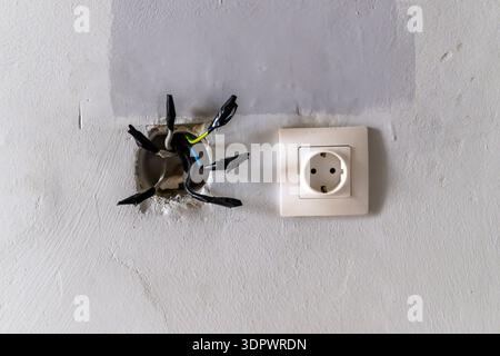 Exposed electrical wires in wall hole next to socket, unsafe installation, selective focus Stock Photo