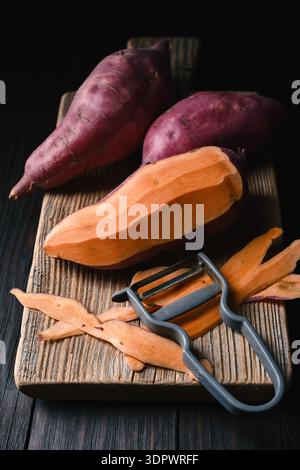 Sweet potato sliced on wooden board with peeler. Healthy cooking preparation concept Stock Photo