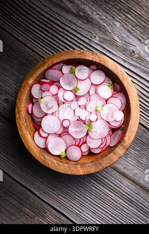 Sliced radishes in wooden bowl on rustic plank background, top view. Natural salad ingredients for seasonal cooking and eco lifestyle Stock Photo