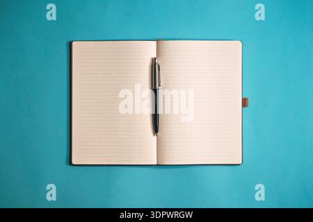 Open lined notebook with pen centered on blue background, minimalist flat lay composition symbolizing planning, writing, organization, and productivit Stock Photo