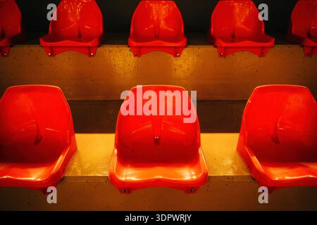 Rows of bright red plastic stadium seats arranged symmetrically on concrete steps under warm lighting, creating a bold geometric pattern and repetitio Stock Photo