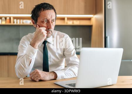 Thoughtful businessman sitting in home office with chin on fist, showing deep reflection, focus, and careful decision making in a professional environ Stock Photo