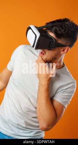 Man uses virtual reality headset in a bright orange room while showing surprise Stock Photo