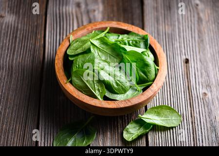 Bright leafy spinach arranged in wooden bowl on weathered wooden table close up. Fresh vegetables, sustainable lifestyle and healthy eating concept Stock Photo