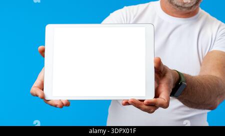 Man shows blank tablet screen against blue background in indoor setting Stock Photo