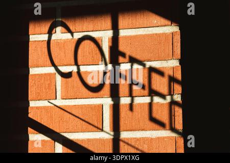 Shadow of a COFFEE sign cast on a red brick wall in warm sunlight, creating bold typography and geometric patterns Stock Photo