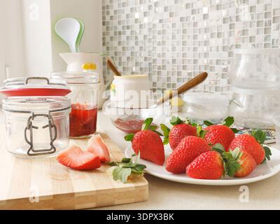 Composition of fresh strawberries and empty jars in kitchen. Seasonal farm produce and homemade preserves. Design backdrop. Stock Photo