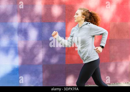 Woman Runs on Street Next to Colorful Wall During Daylight in Urban Setting Stock Photo