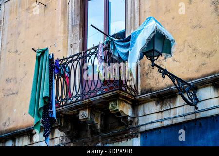 Laundry drying on wrought iron balcony of ochre building in Catania historic centre, Italy. Stock Photo