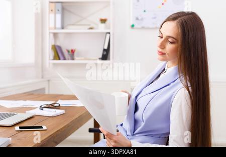 Woman Examines Documents While Sitting at a Desk in a Bright Office Space Stock Photo