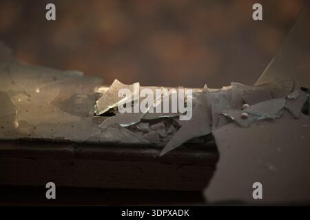Broken Glass on Window Sill Sharp shards of shattered window glass illuminated by warm light in abandoned interior Stock Photo