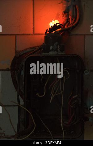 Old fuse box with exposed wires and glowing damaged socket creating dangerous fire hazard indoors Stock Photo