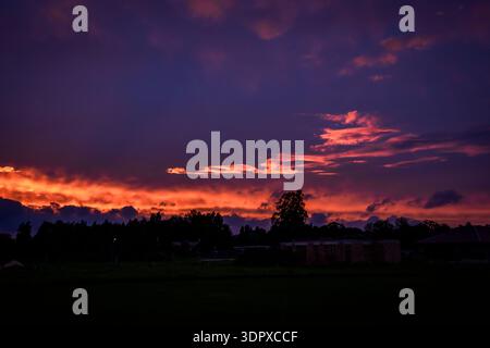 Dramatic purple and orange sunset sky over a dark rural silhouette at twilight. Stock Photo