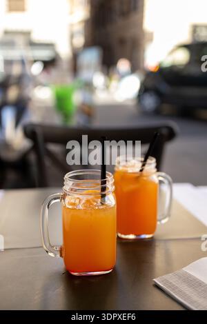 Two mason jars filled with fresh orange juice served on a table at an outdoor cafe in the historic center of Rome with blurred city street background Stock Photo