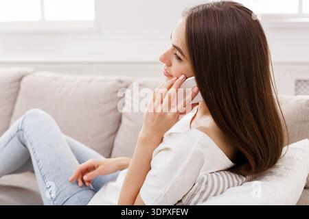 Woman Sitting on Sofa Talking on Mobile Phone While Relaxing in a Room Stock Photo