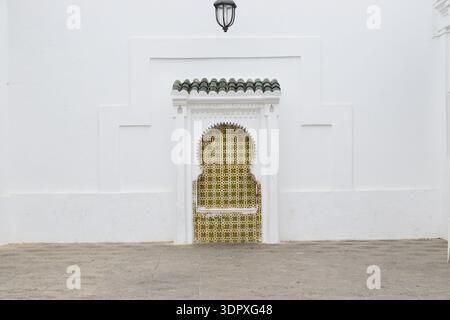 Symmetrical architectural study of a traditional Moorish arched niche featuring geometric patterned tiles and a hanging vintage metal lantern on a min Stock Photo