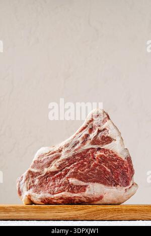 Close-up of a raw ribeye steak with marbled texture, placed on a wooden board. The steak's rich marbling indicates high-quality, perfect for grilling Stock Photo