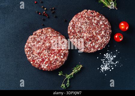 Two raw veal burger patties on a dark background, garnished with fresh rosemary, cherry tomatoes, and peppercorns. Perfect for recipes or culinary pre Stock Photo