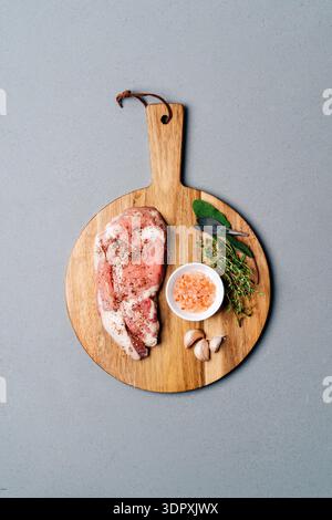 A raw ribeye steak seasoned with pepper, garlic, and herbs, placed on a rustic wooden cutting board. Accompanied by fresh thyme, sage leaves, and Hima Stock Photo