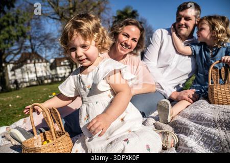 A joyful family sits on a picnic blanket enjoying the Easter holiday. Children hold baskets filled with colorful eggs, capturing the essence of spring Stock Photo