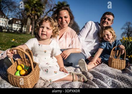 A joyful family sits on a picnic blanket enjoying the Easter holiday. Children hold baskets filled with colorful eggs, capturing the essence of spring Stock Photo