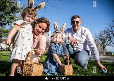 A joyful family participates in an Easter egg hunt during springtime. Children with bunny ears eagerly search for colorful eggs, creating cherished ho Stock Photo