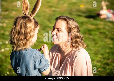 A joyful family moment during Easter, with a woman and child wearing bunny ears in a sunny park, embracing the festive spring atmosphere while enjoyin Stock Photo