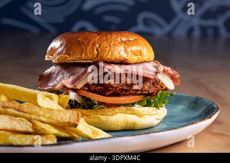 Delicious crispy chicken burger topped with bacon, cheese, fresh tomato, and lettuce, served with a side of golden fries. A perfect meal for burger lo Stock Photo