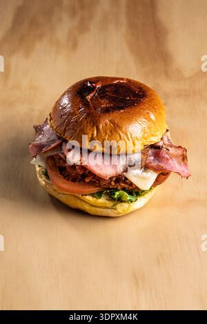 Delicious crispy chicken burger topped with savory bacon, melted cheese, fresh tomato, and lettuce in a golden bun, offering a hearty and flavorful me Stock Photo