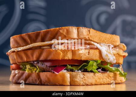 Mouthwatering ham and cheddar sandwich stacked with crispy fried egg, fresh lettuce, juicy tomato, and sliced onion, served on toasted bread for a del Stock Photo