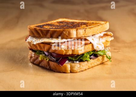 Delicious ham and cheddar sandwich featuring a perfectly fried egg, fresh lettuce, juicy tomato, and crisp onion, creating a mouthwatering combination Stock Photo