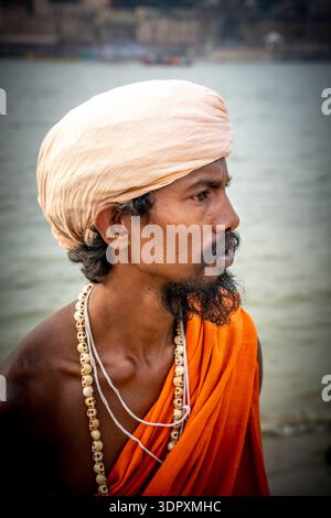 Profile of a Sadhu with a turban and bead necklace dressed in orange by the river in India. Stock Photo
