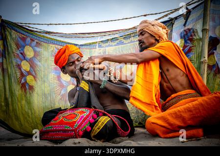 Two Indian men dressed in orange perform a ritual with vibrant fabric and beads in a cultural setting. Stock Photo