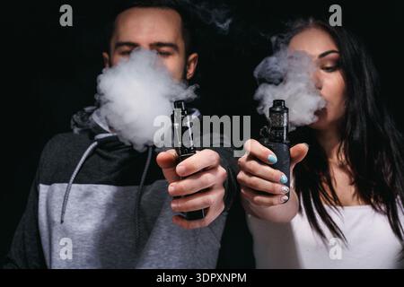 blow smoke and vape Couple Vaping Blowing in a Dark Room During an Indoor Gathering Stock Photo Vape Flavor:Strawberry Savers BRAND_STLTH X GEEK BAR Why A Disposable Vape