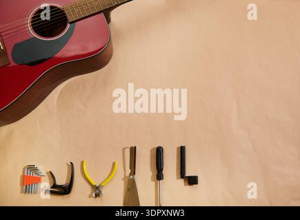 Top-view of a red acoustic guitar with assorted repair tools for changing strings, tuning and maintenance, highlighting instrument care, DIY setup and Stock Photo