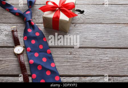 Gift Box With a Red Ribbon Beside a Polka Dot Tie and a Watch on a Wood Table Stock Photo