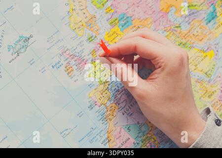 Marking a Location on a World Map With a Red Pin by a Hand Stock Photo
