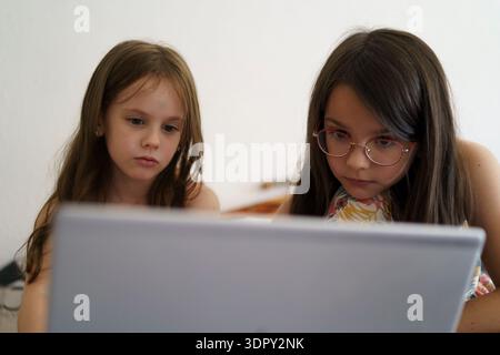Two girls looking at a laptop screen together, focused and engaged, modern education and digital learning concept showing real life childhood Stock Photo