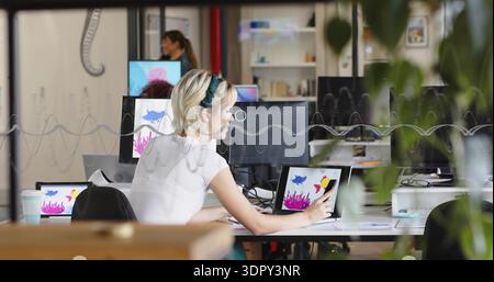 Drawing woman in white top and hairband using stylus on laptop or tablet in studio, waveform partiti Stock Photo