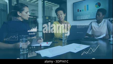 Discussing three women wearing yellow, dark, pink tops reviewing data at meeting table with laptop Stock Photo