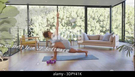 Doing woman twisting lunge on blue mat in sunny living room, wearing workout set, dumbbells, watch Stock Photo