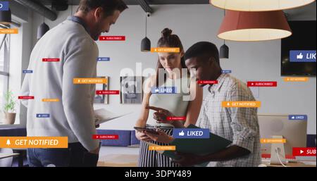 Reviewing three coworkers leaning over tablet in open-plan office, pointing at device with overlays Stock Photo