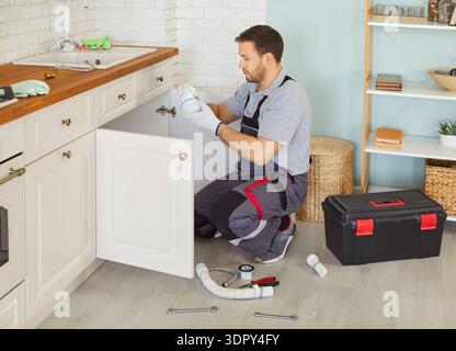 Man plumber in uniform with toolbox replacing the water filter or fixing broken pipe in kitchen. Stock Photo