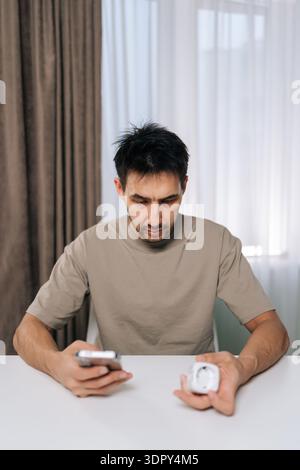 Vertical portrait of man connecting smart home device using smartphone, looking at application settings, setting up and controlling smart socket from Stock Photo
