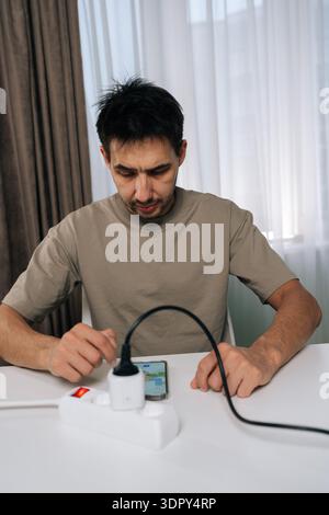 Vertical portrait of man controlling smart socket device connected to power strip using mobile phone application for home automation, managing energy Stock Photo