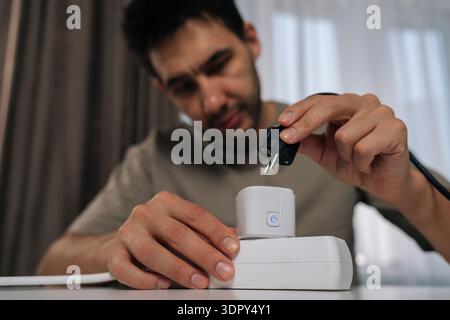 Portrait of young man plugging smart socket into power strip, controlling energy consumption and automating home appliances for energy efficiency and Stock Photo